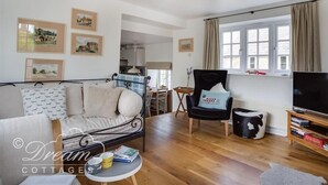A cozy living room with a sofa, a chair, a TV, and framed pictures on the wall. - The Old Reading Room (Weymouth)