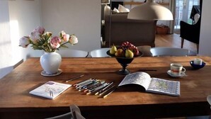 A wooden dining table with a vase of flowers, a fruit bowl, and a book. - The Old Reading Room (Weymouth)