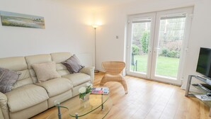 Ett vardagsrum med en beige soffa, ett soffbord i glas, en fåtölj i rotting och en tv som står på ett TV-bord.