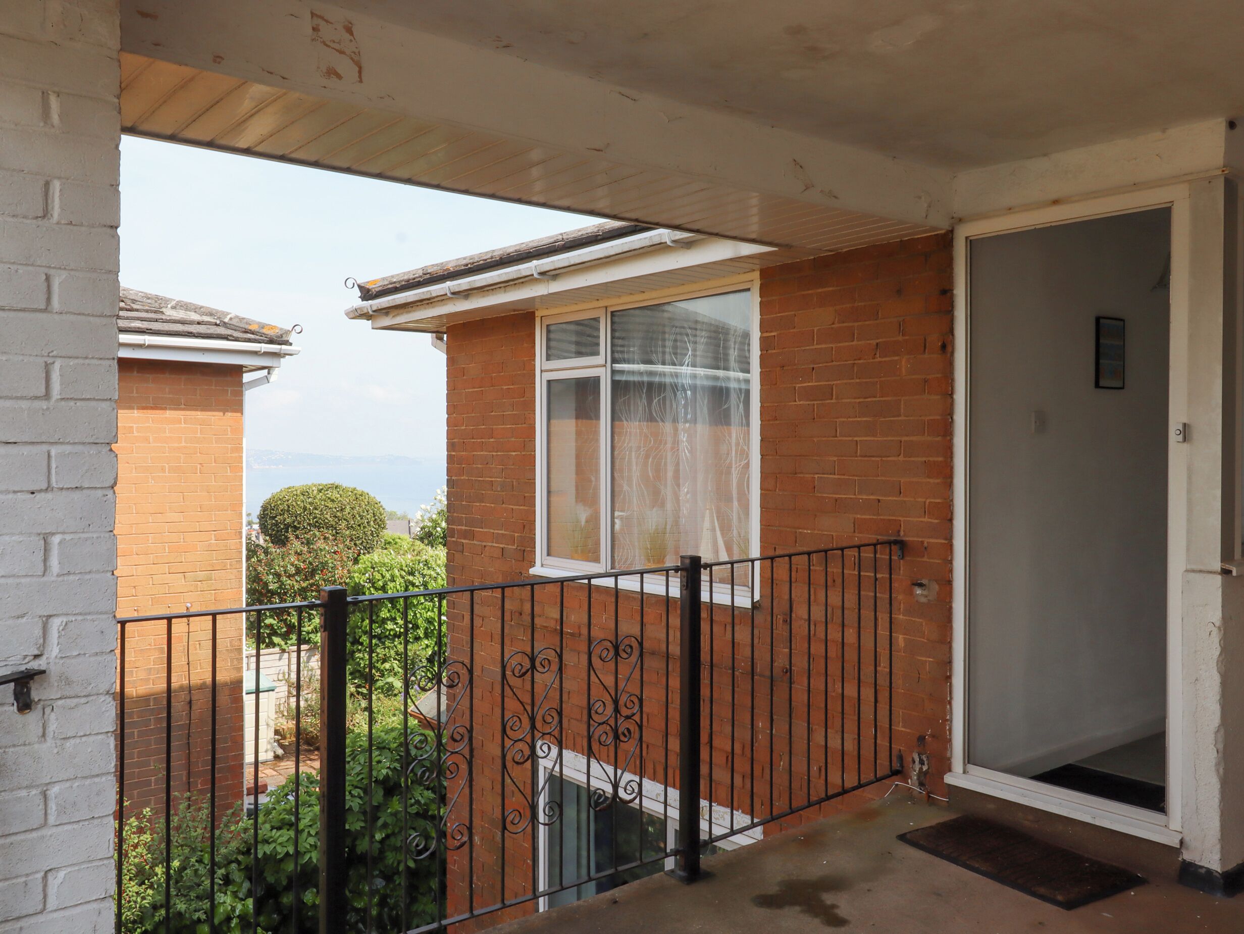 A balcony with a metal railing, a door, and a window with a curtain.