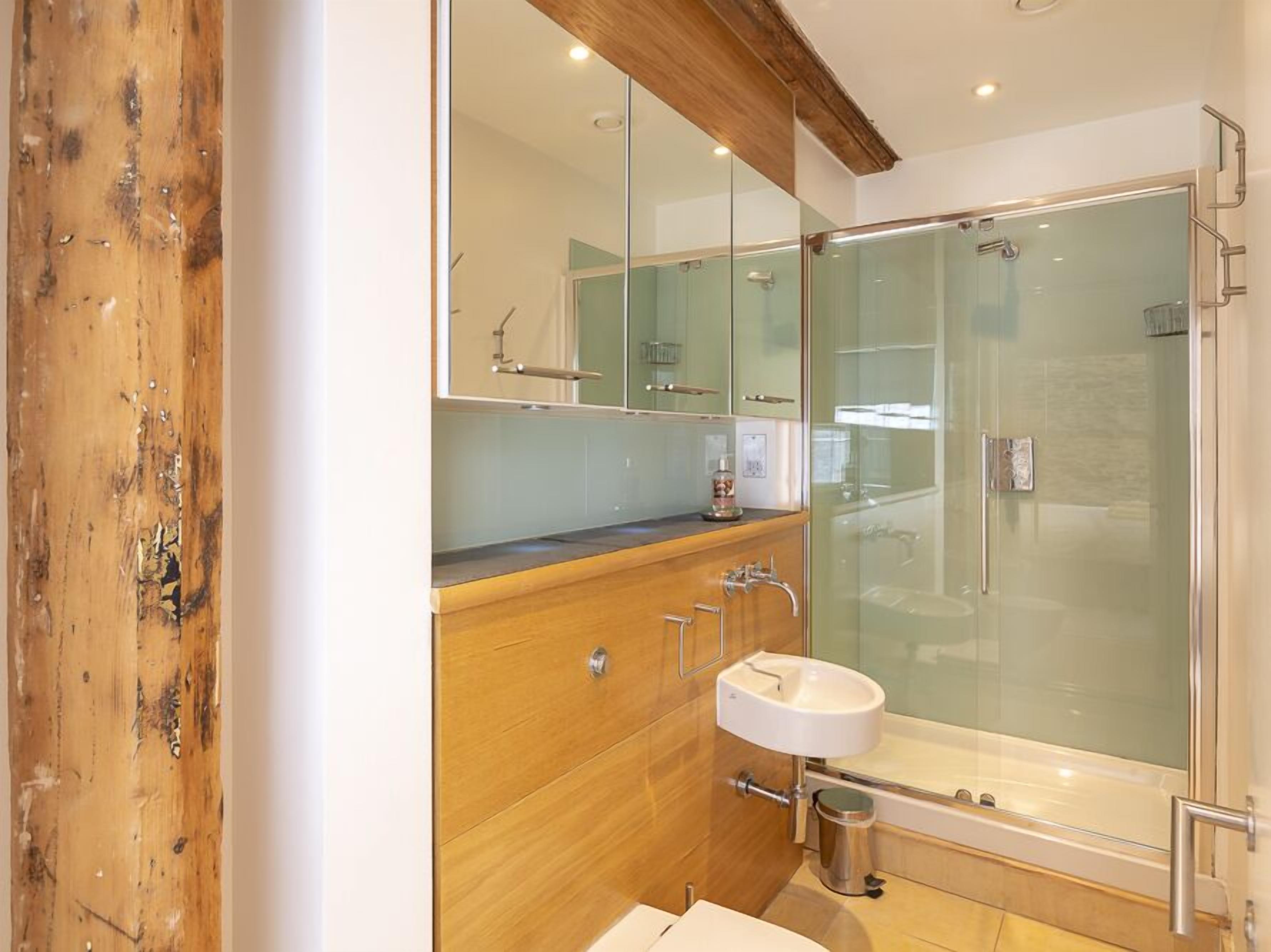A modern bathroom with a wooden vanity, a glass shower enclosure, and a white sink.