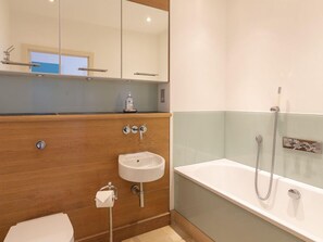 A modern bathroom with a wooden vanity, a white sink, a toilet, and a bathtub with a shower. - 8 The Pottery (Dartmouth)