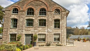 A stone building with a central entrance, multiple windows, and a paved area in front.