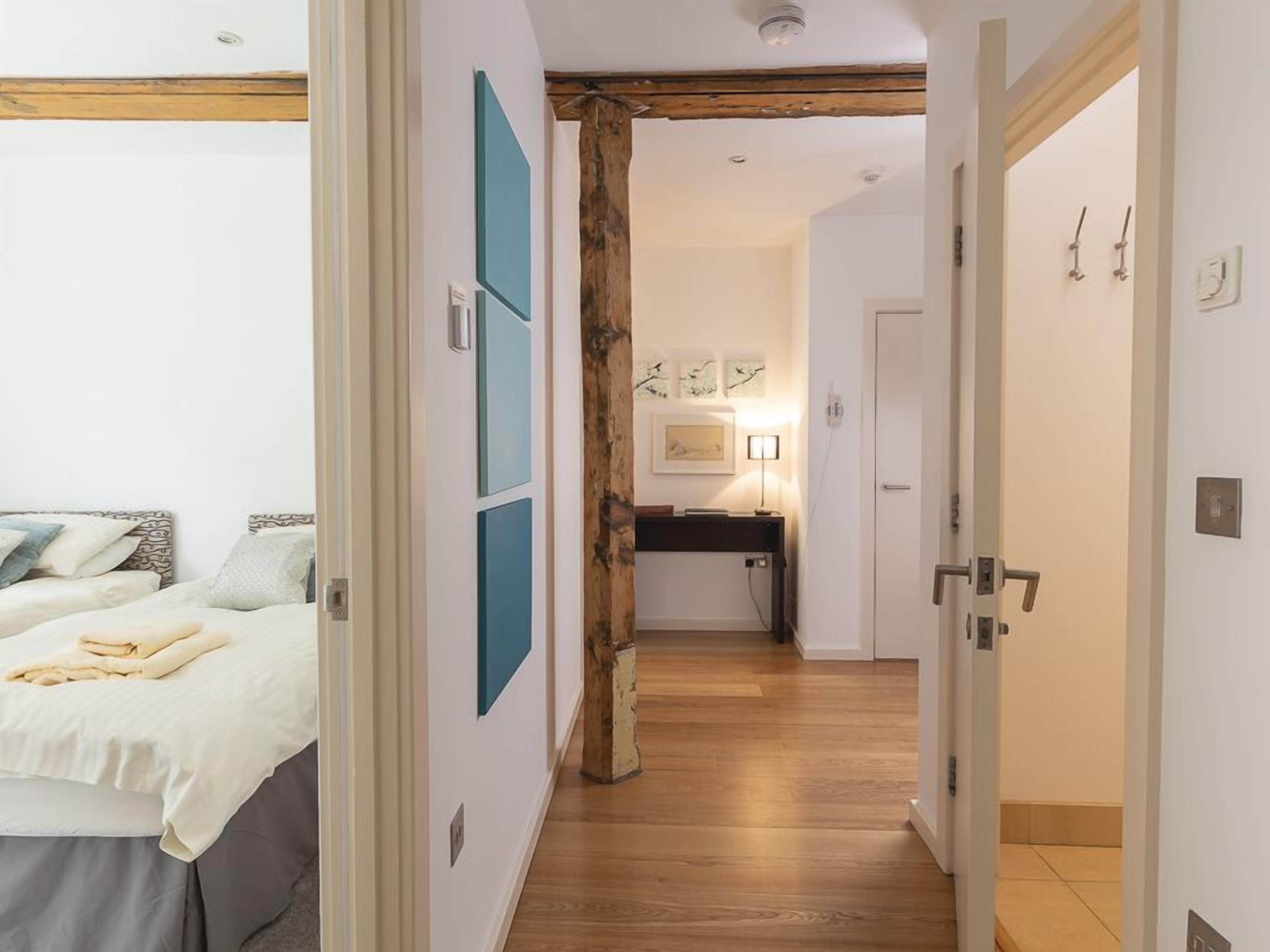 A bedroom with a bed, a desk, and a chair. There is a wooden beam on the ceiling and a door with a handle.