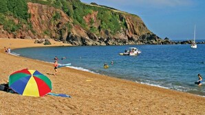 A beach with a colorful umbrella, calm water, and boats.