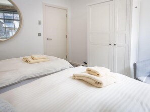 A hotel room with two beds, each with a neatly folded towel. There is a round mirror on the wall, a white door, and a wardrobe. - 8 The Pottery (Dartmouth)