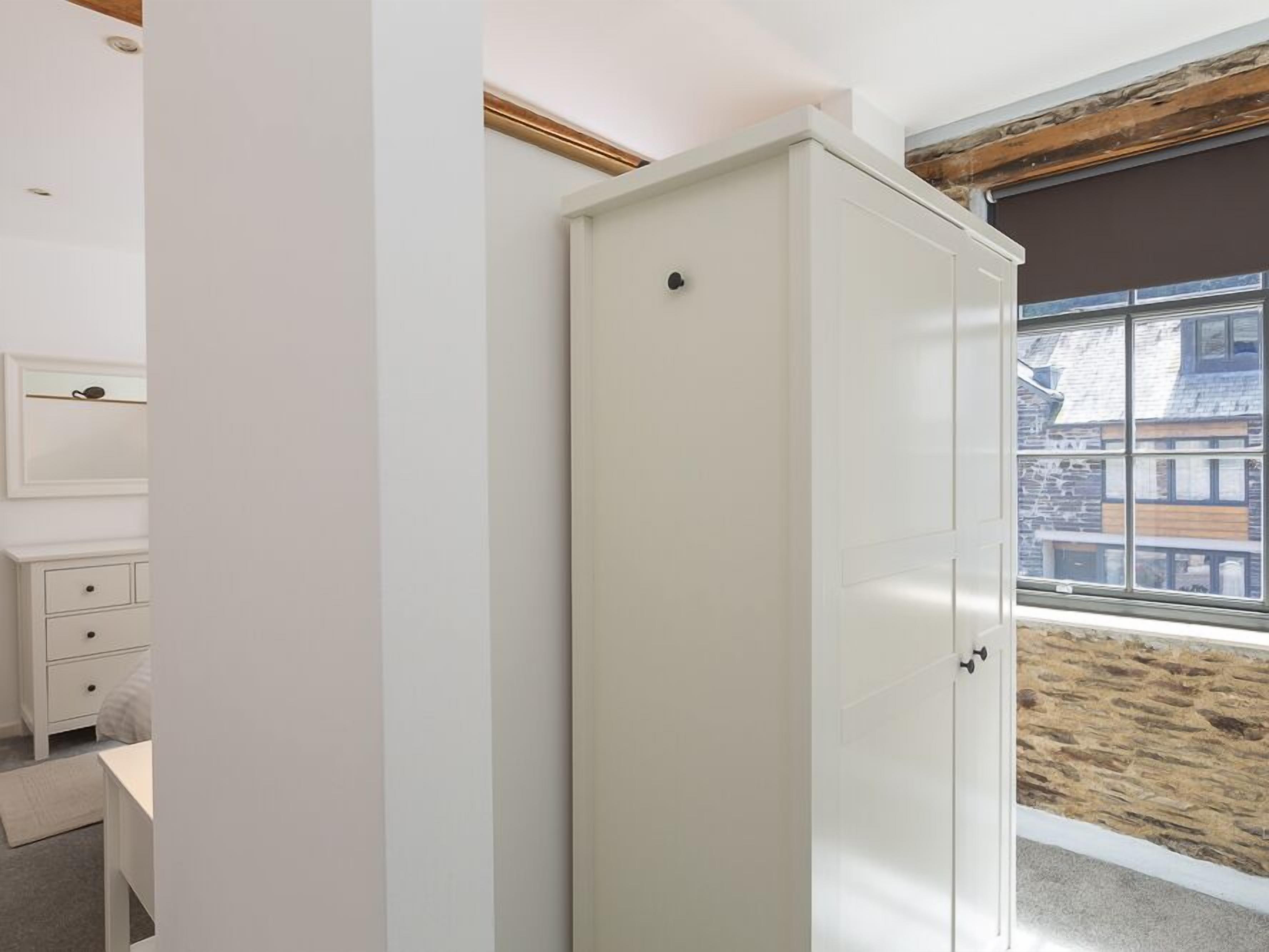 Ein Schlafzimmer mit großem Kleiderschrank, Nachttisch, Kommode und Fenster mit Blick auf Gebäude.