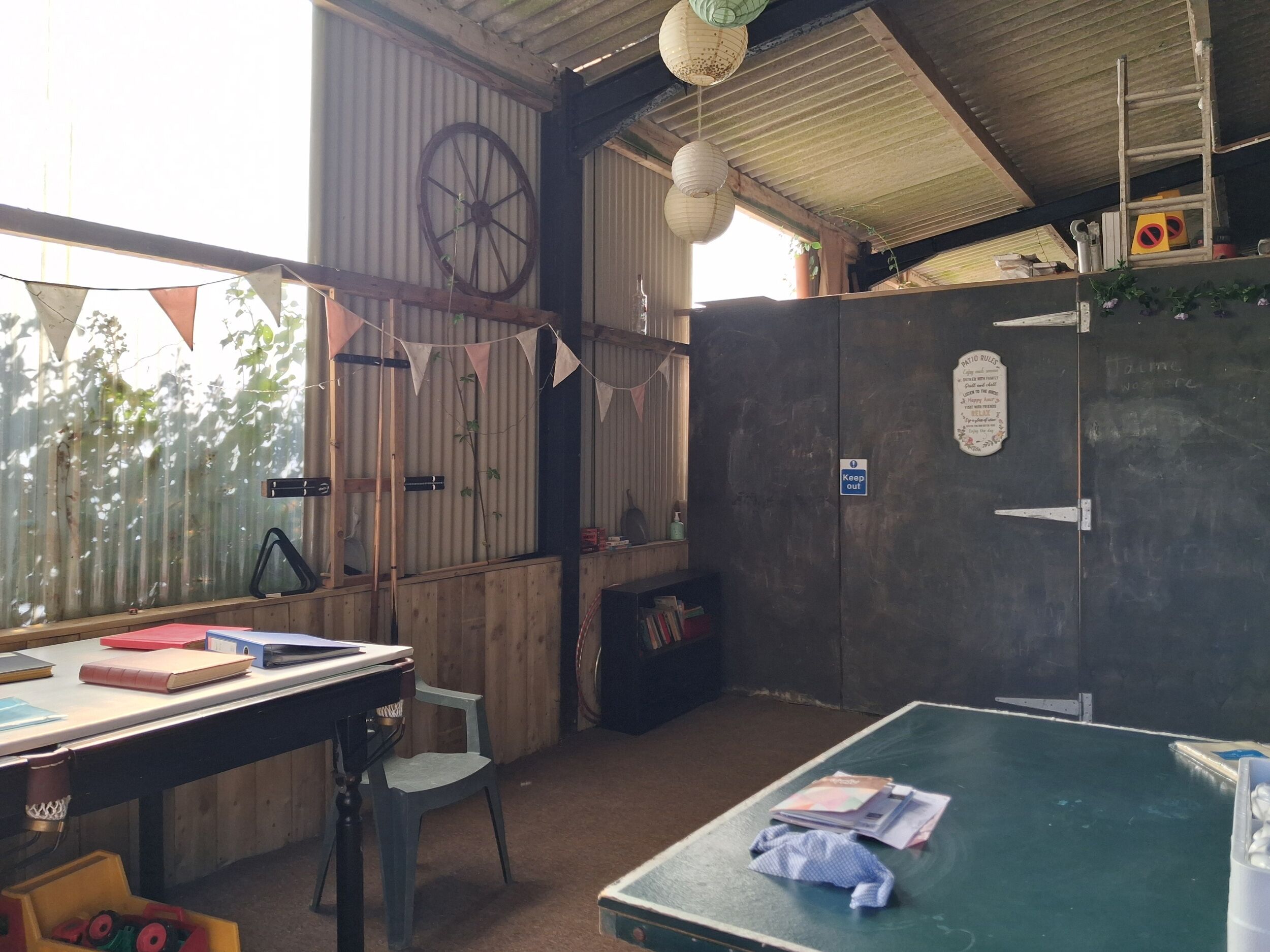 A rustic room with a wooden desk, a green table, and a 'Keep out' sign on a door.