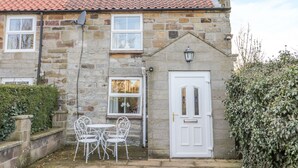 A stone house with a red-tiled roof, a white door, and a small garden with white metal chairs. - Dove Cottage (Whitby)