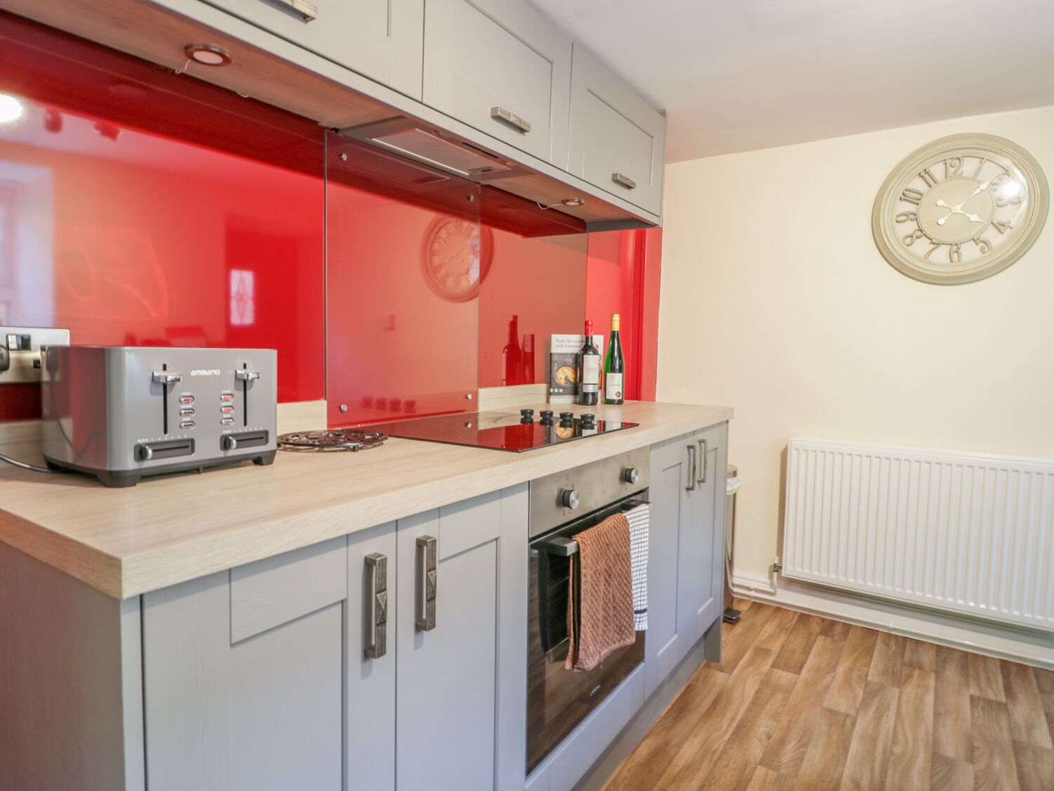 Une cuisine moderne avec un revêtement mural rouge, des appareils électroménagers en acier inoxydable et une horloge murale.