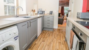 A compact kitchen with a washing machine, microwave, and a small dining area visible through an open door. - Dove Cottage (Whitby)