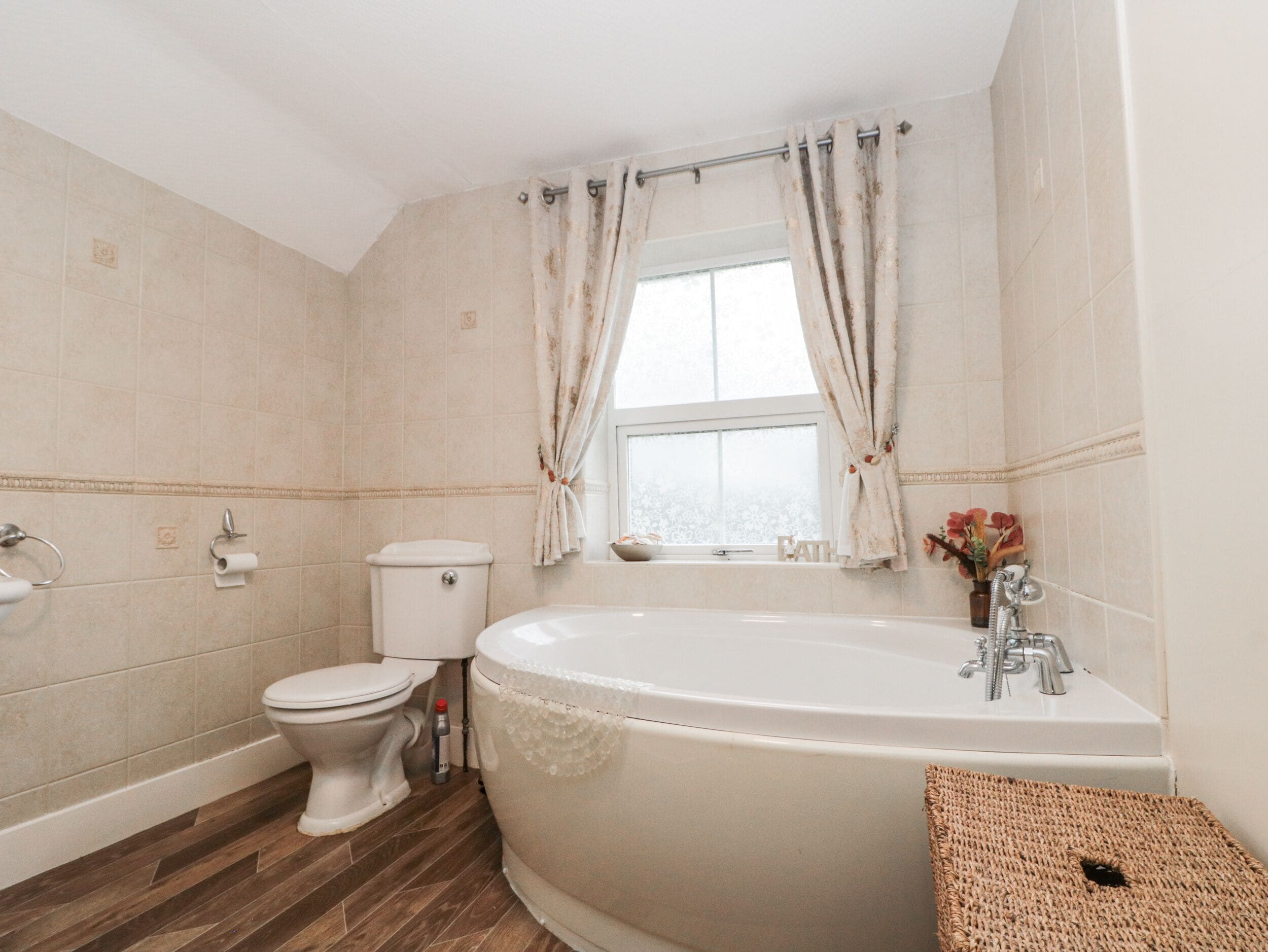 A bathroom with a toilet, a bathtub, and a window with curtains.