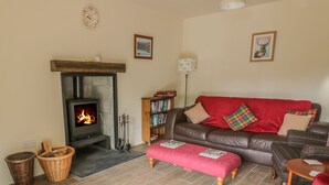 A cozy living room with a fireplace, a leather sofa, a red ottoman, and a bookshelf. - Fois House (Callander)