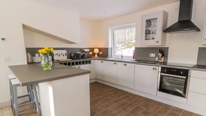 A modern kitchen with white cabinets, a central island, a built-in oven, and a window providing natural light. - Fois House (Callander)