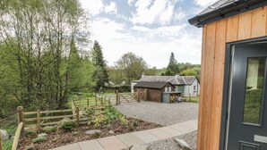 A rustic building with a wooden exterior and a gravel driveway leading to a fenced garden area. - Fois House (Callander)