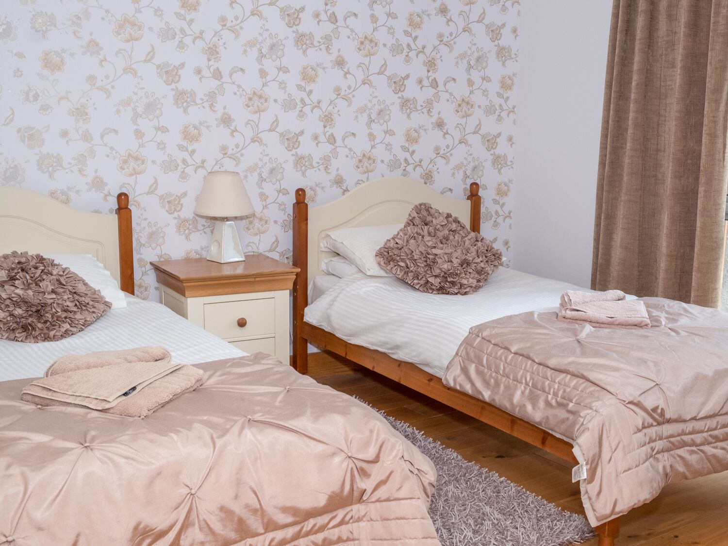 A bedroom with two beds, a nightstand with a lamp, and floral wallpaper.
