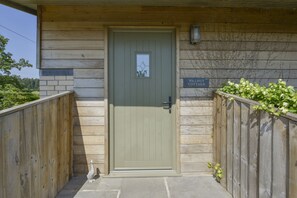 A wooden cottage with a green door, a sign reading "Walnut Cottage," and a small garden area with a wooden fence and greenery. - Walnut Cottage (Newton Abbot)