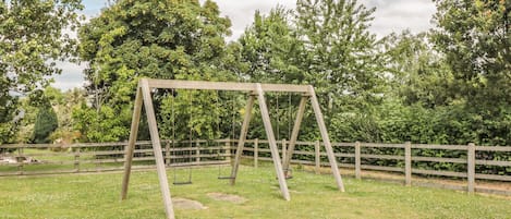 A wooden swing set in a grassy area with a wooden fence and trees in the background.