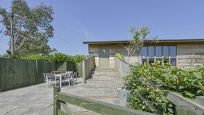 A building with a wooden exterior, a front door, and a staircase leading to the entrance. There is a patio area with a table and chairs.