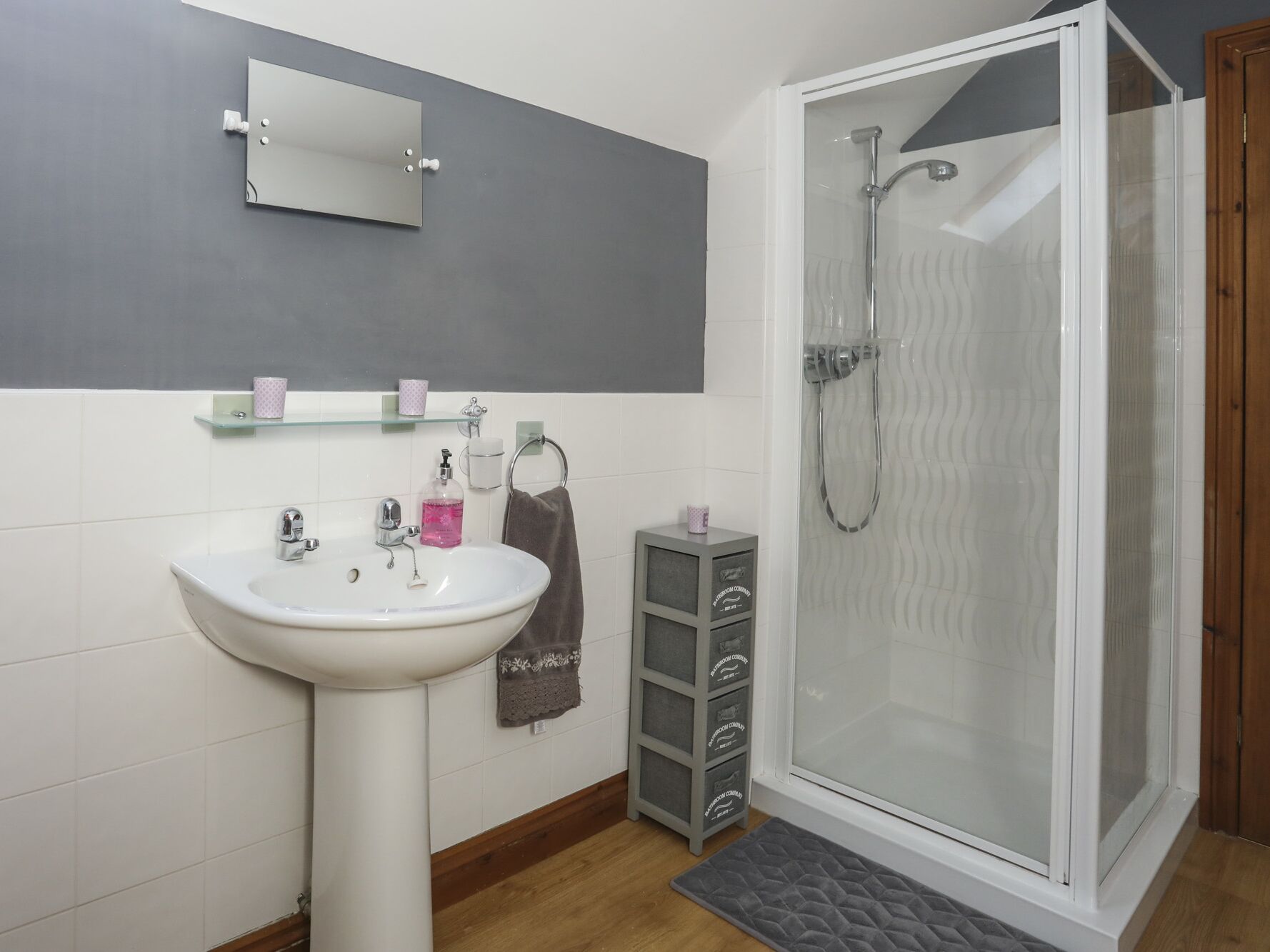 Un baño con un lavabo blanco, una cabina de ducha de vidrio y un espejo sobre el lavabo.