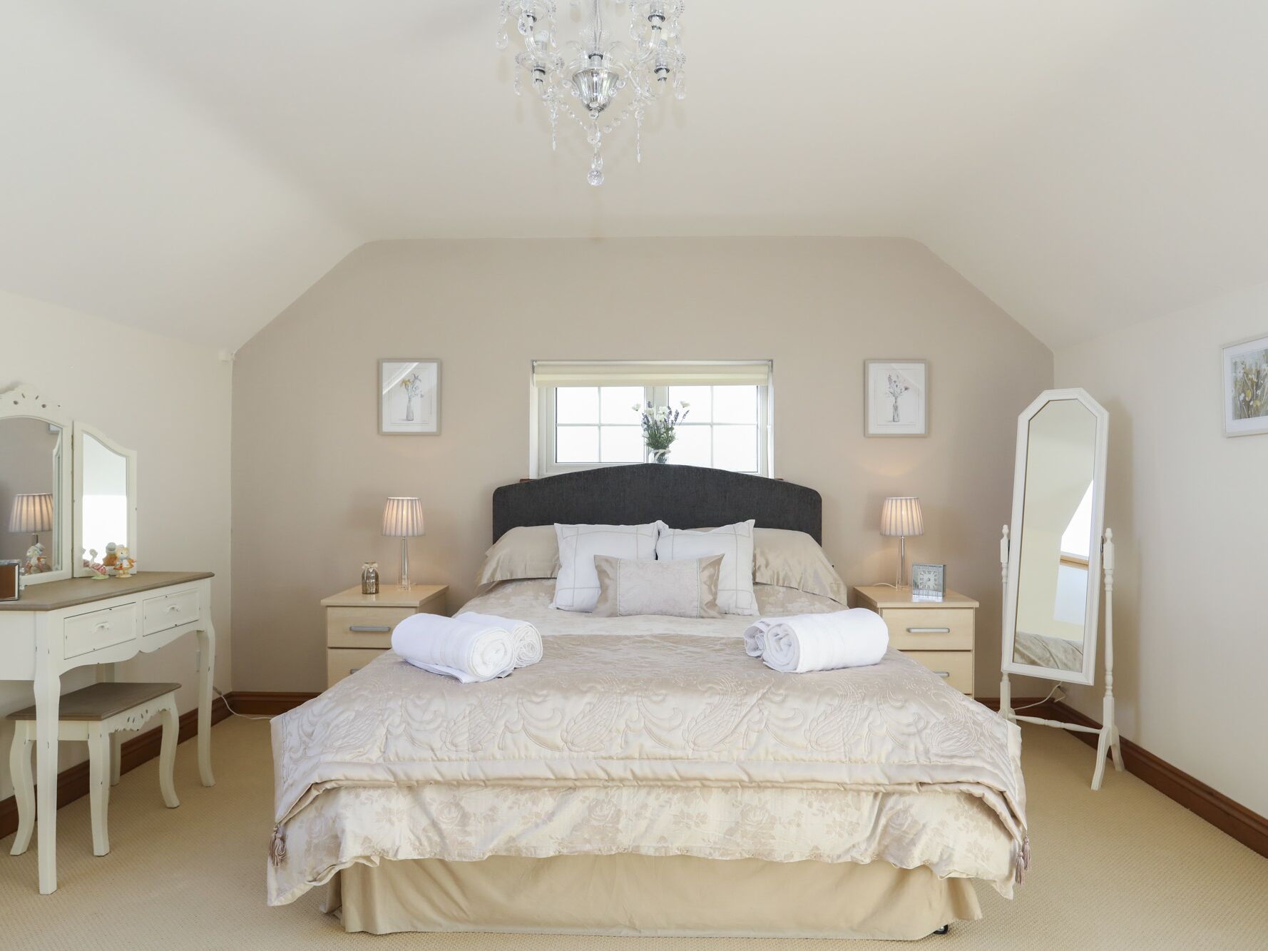 Een slaapkamer met een groot bed, een dressoir, een spiegel en een kroonluchter.