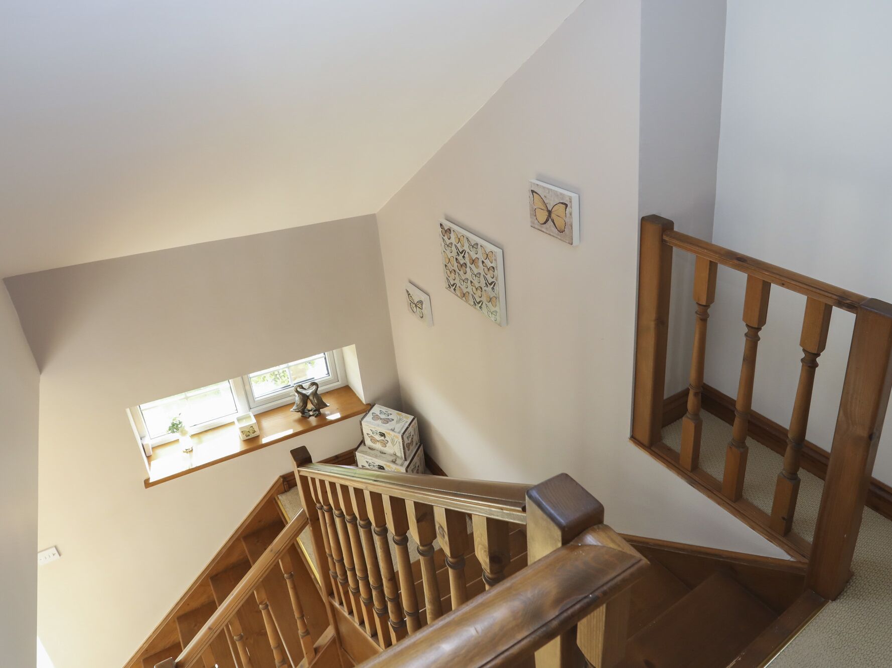 A wooden staircase with a handrail, a window with a plant, and wall decorations including a butterfly and a heart pattern.