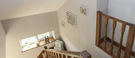 A wooden staircase with a handrail, a window with a plant, and wall decorations including a butterfly and a heart pattern.