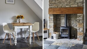 Un comedor con mesa y sillas de madera, un jarrón con flores y una chimenea de piedra con estufa de leña.