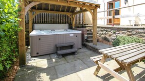 Un jacuzzi bajo una pérgola de madera, una pared de piedra y una mesa de picnic de madera.