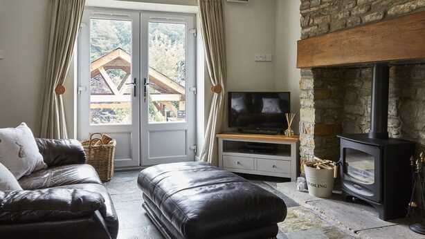 Una sala de estar acogedora con chimenea de piedra, sofá de cuero y televisor sobre un mueble de madera.
