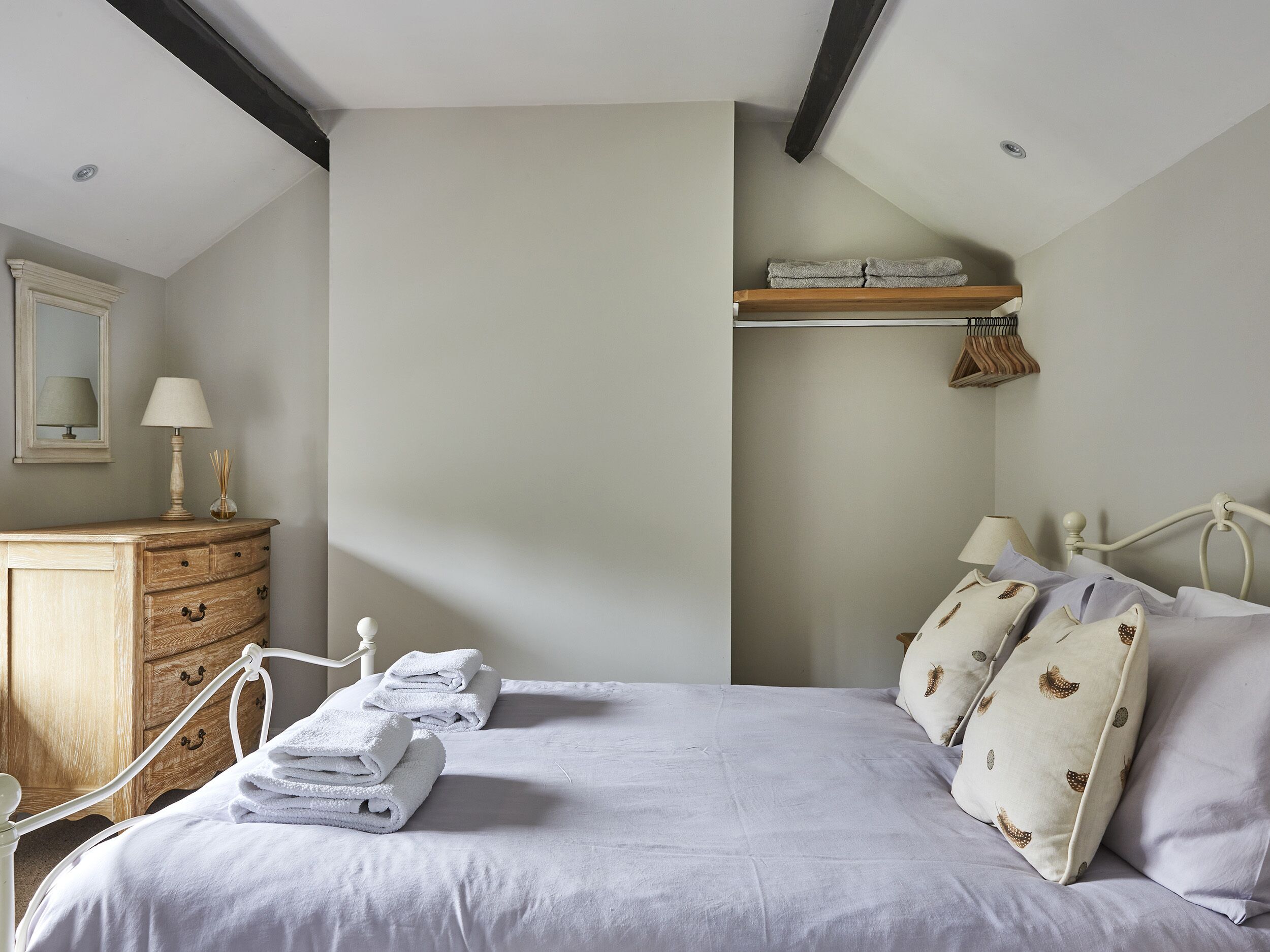 A bedroom with a bed, a nightstand, a dresser, and a shelf with towels.
