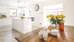 A modern kitchen with white cabinetry, a wooden island, and a dining table set with white mugs and a vase of yellow flowers. - The Gables (Holyhead)