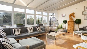 A spacious living area with a large sofa set, a hanging chair, and a coffee table. - The Gables (Holyhead)