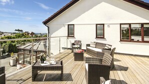 A rooftop terrace with wicker furniture, a glass balustrade, and a view of the sea. - The Gables (Holyhead)