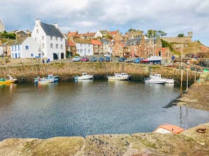 A coastal town with stone buildings, a harbor with several boats, and a stone wall. - Sandpipers (Anstruther)