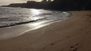 En strand där solljuset reflekteras i vattnet, en sandstrand och byggnader i bakgrunden.