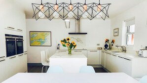 Ett modernt kök med vita skåp, ett vitt matbord och en geometrisk lampa.