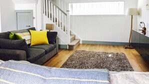Ett modernt vardagsrum med en trappa, en soffa med kuddar, en mönstrad matta och en lampa.
