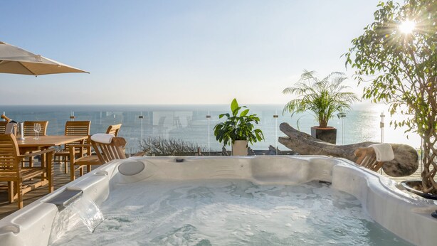 A hot tub with a city view, wooden furniture, and potted plants.