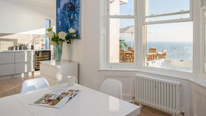 A modern kitchen with white cabinets, a dining area with a white table, and a large window overlooking the sea.