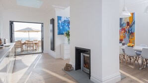 A spacious living room with a fireplace, a dining area, and a view of the sea.