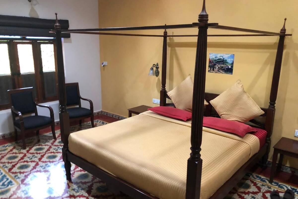 A four-poster bed with a red and beige bedspread, wooden headboard, and a small table beside it.