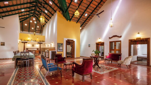 A spacious lobby with a high ceiling, a dining area with a long table and chairs, and a seating area with sofas and a coffee table. - amã Stays & Trails, Rare Earth Estate - Coorg (Madikeri)