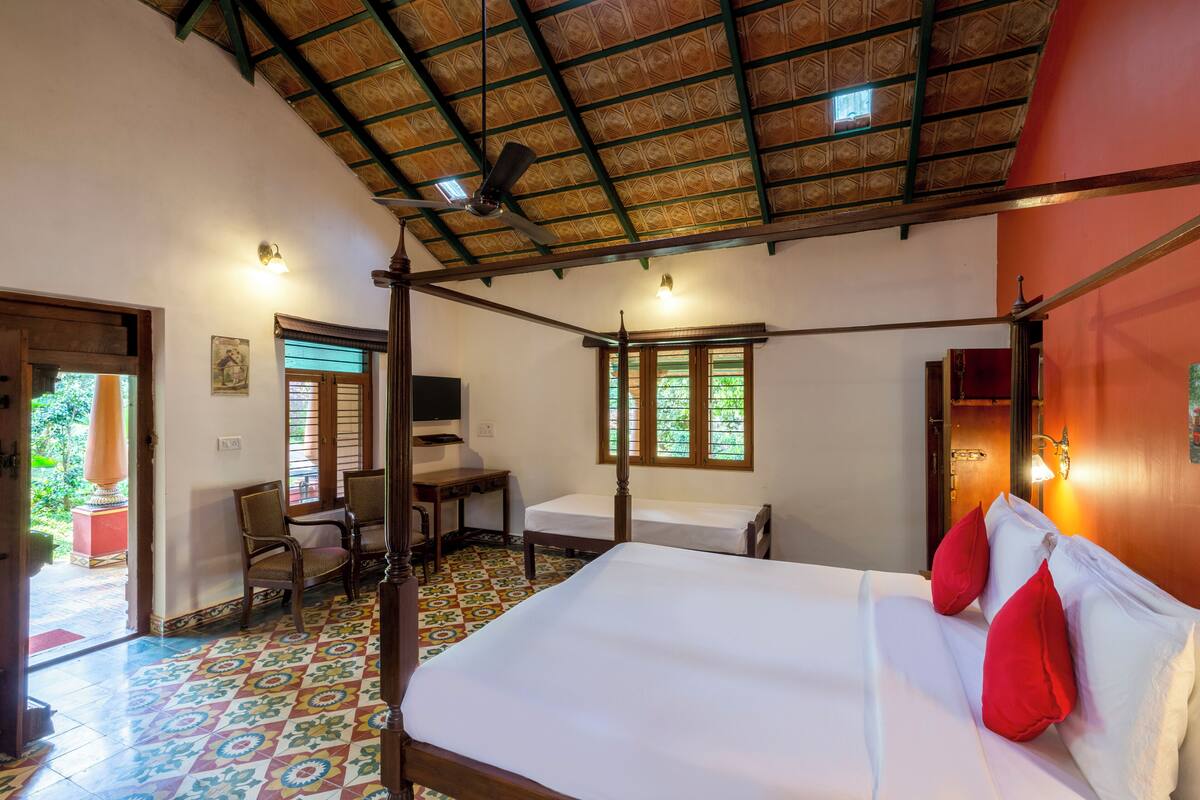 A room with a bed, two chairs, a desk, and a ceiling fan.