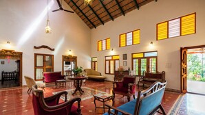 A spacious room with traditional furniture, large windows with wooden shutters, and a high ceiling with exposed beams. - amã Stays & Trails, Rare Earth Estate - Coorg (Madikeri)