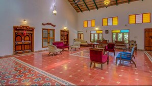 A spacious room with a high ceiling, traditional wooden furniture, and patterned floor tiles. - amã Stays & Trails, Rare Earth Estate - Coorg (Madikeri)