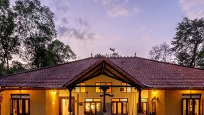 A building with a tiled roof, a central entrance, and a fountain in the courtyard. - amã Stays & Trails, Rare Earth Estate - Coorg (Madikeri)