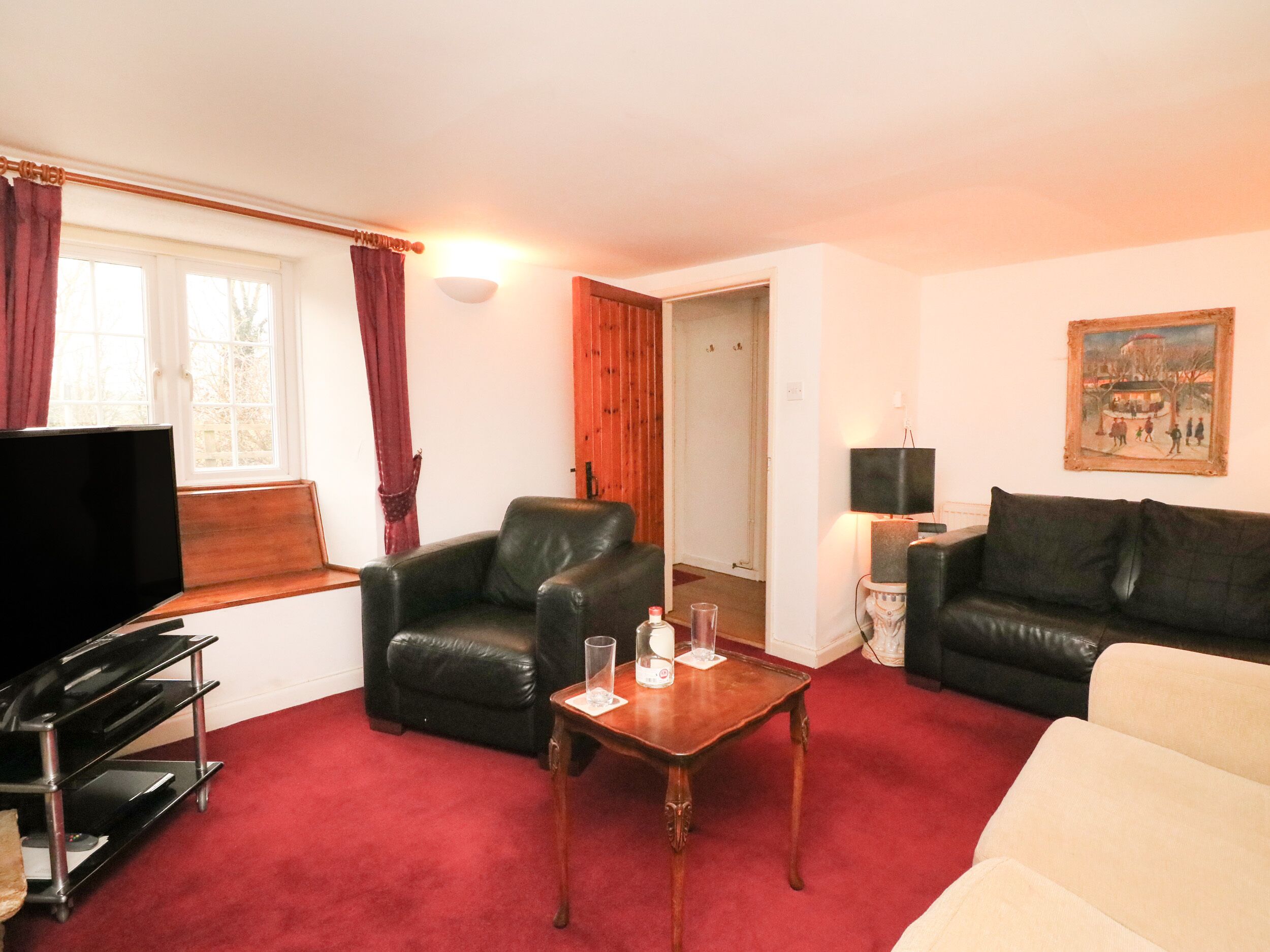 A living room with a TV, leather chairs, a wooden coffee table, and a red carpet.