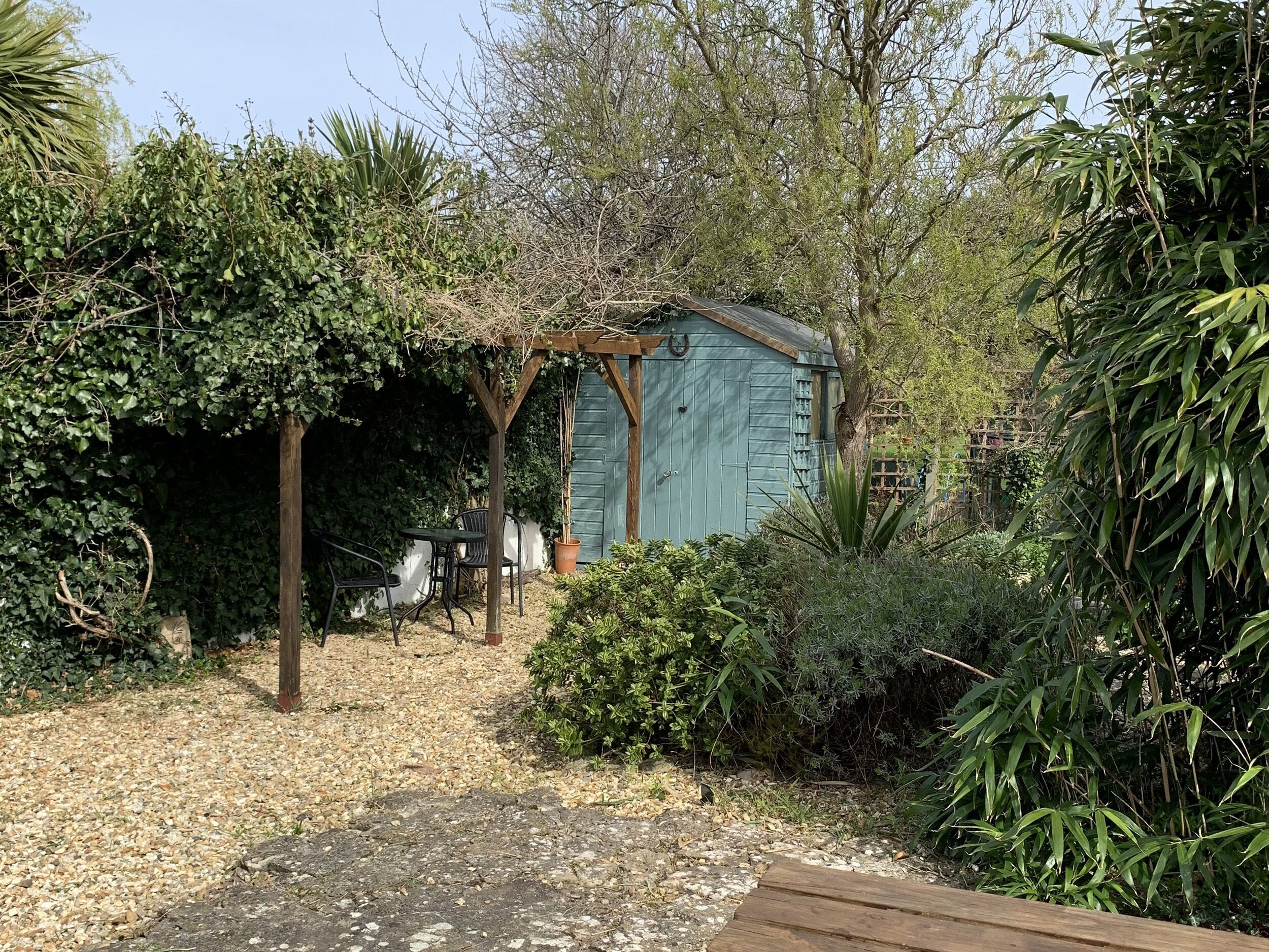 A garden with a wooden pergola, a shed, and a gravel path.