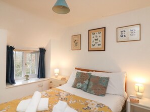 Een slaapkamer met een bed, een raam met gordijnen, een nachtkastje met een lamp en wanddecoratie.